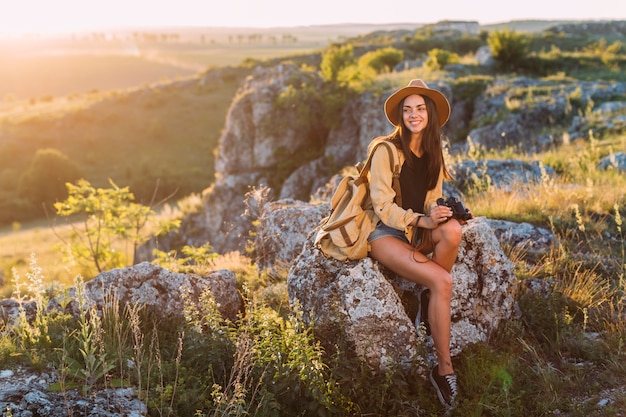 Free photo young smiling woman sitting on rock holding binocular