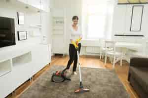 Free photo young smiling woman vacuum cleaning the carpet