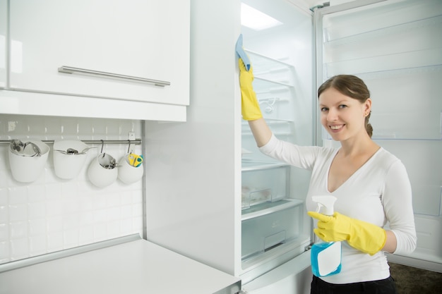 Free photo young smiling woman wearing rubber gloves cleaning the fridge