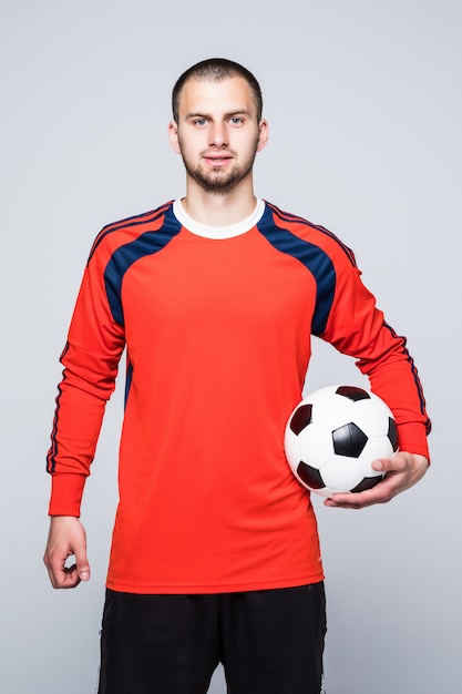 Free photo young soccer player with ball under hand dressed in red jersey in front of white