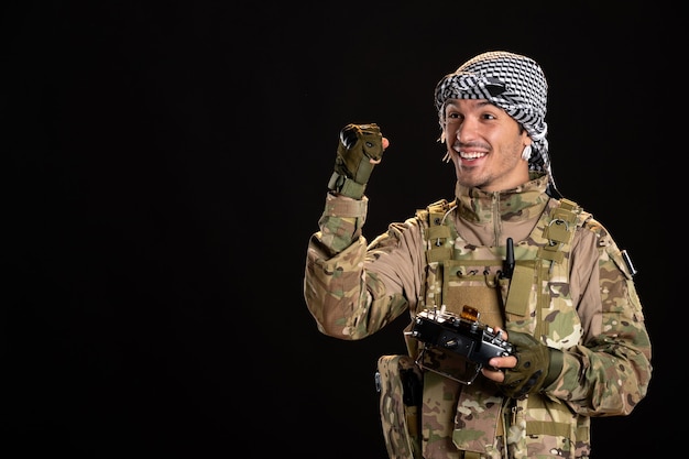 Free photo young soldier in camouflage using remote controller on a black wall