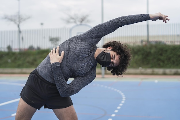 Free Photo young spanish male wearing a black mask is doing a stretching exercise