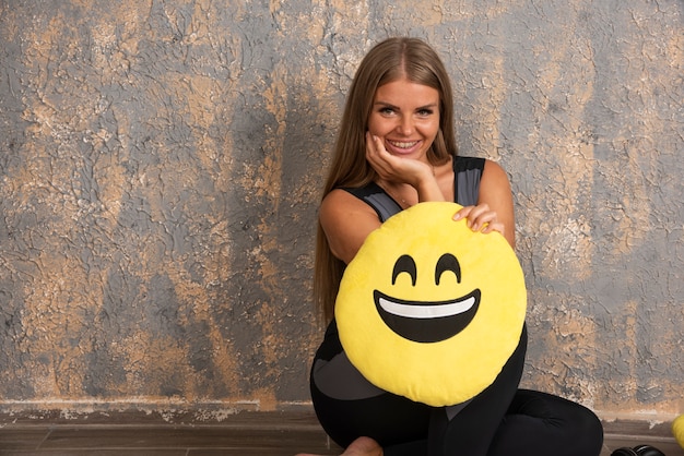 Young sportive girl in sport outfits holding a smiling emoji pillow. 