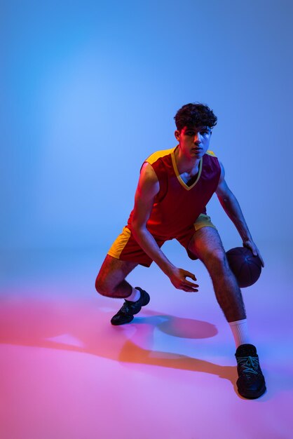 Young sportive man training basketball isolated on gradient in neon