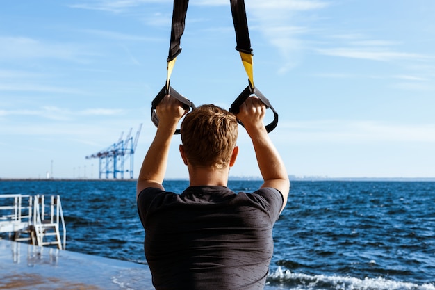 Free Photo young sportive man training with trx near sea in the morning.