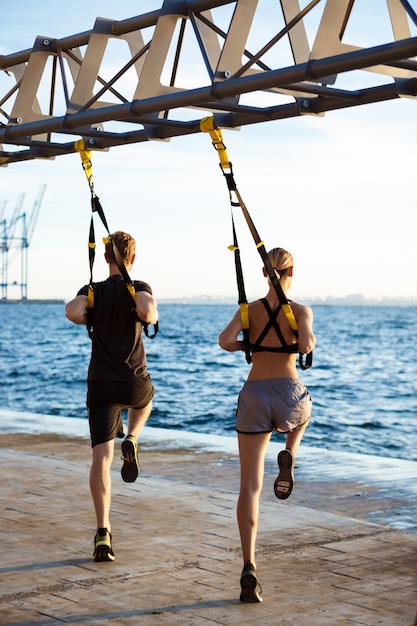 Young sportive people training with trx near sea in the morning.