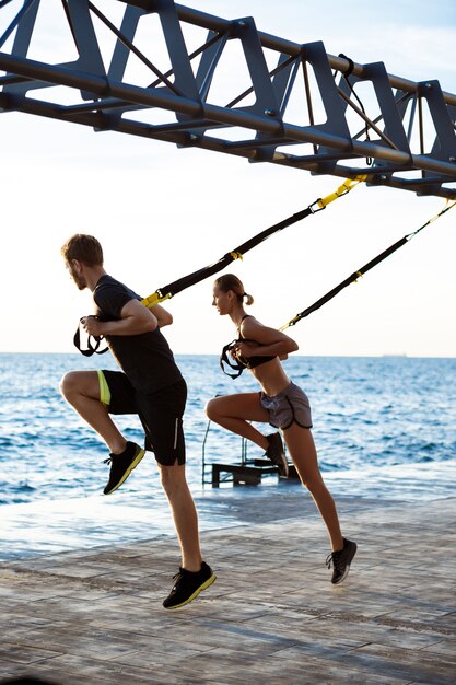 Young sportive people training with trx near sea in the morning.