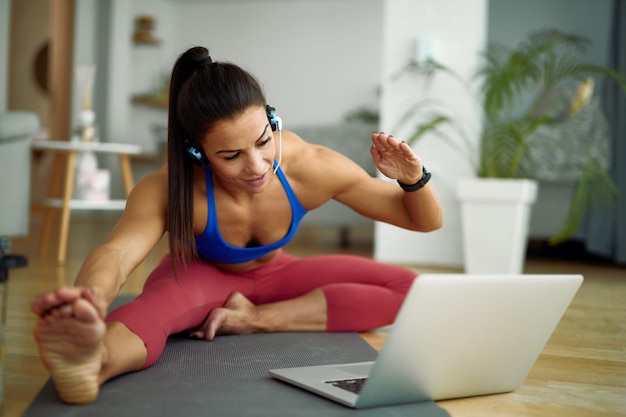 Young sportswoman exercising on the floor while following online exercise class over laptop at home