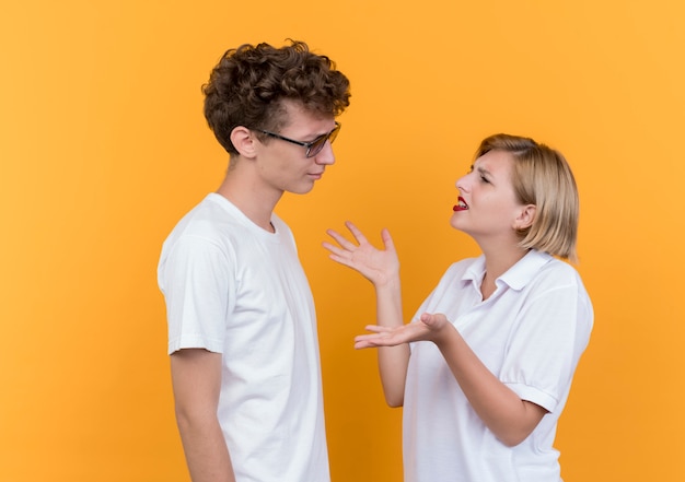 Free photo young sporty couple man and woman looking at each other arguing and quarreling standing over orange wall