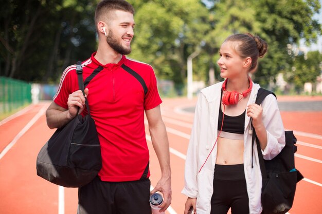 Young sporty man and girl with headphones happily spending time together on treadmill of city stadium