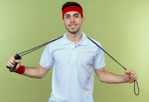 Free photo young sporty man in headband holding skipping rope with smile on face over green