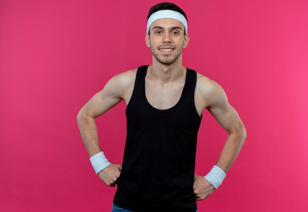 Young sporty man in headband smiling confident over pink