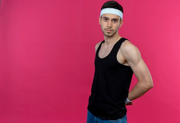 Young sporty man in headband with confident serious expression over pink