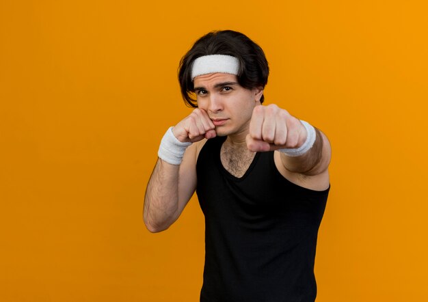 Young sporty man wearing sportswear and headband pointing with fists at camera looking confident 