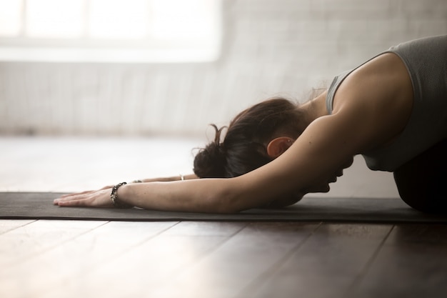 Free photo young sporty woman in balasana pose, white loft studio, closeup