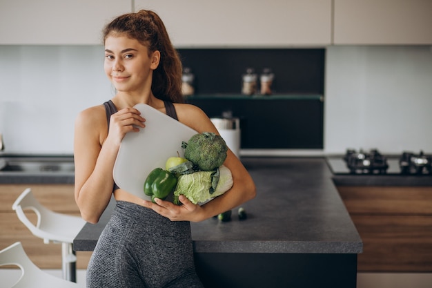 Free photo young sporty woman with scales and vegetables at the kitchen