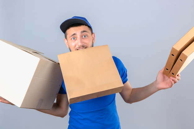 Young over strained delivery man wearing blue polo shirt and cap standing with packages confused over isolated white background