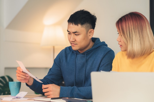 Young stressed asian couple managing finances, reviewing their bank accounts using laptop computer