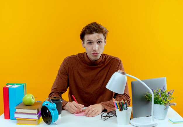 young student boy sitting at desk with school tools writing something 