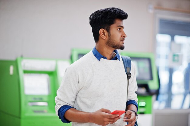 Young stylish asian man with mobile phone and backpack against row of green ATM