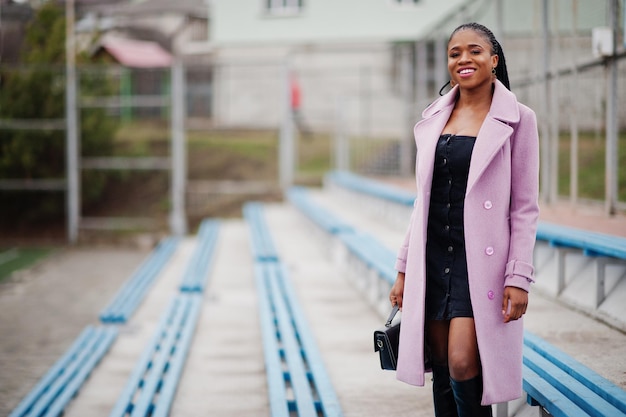 Young stylish beautiful african american woman in street at the stadium bleachers wearing fashion outfit coat hold handbag