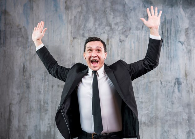 Young stylish businessman raising hands and smiling