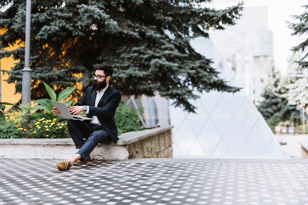 Young stylish businessman sitting in campus using laptop