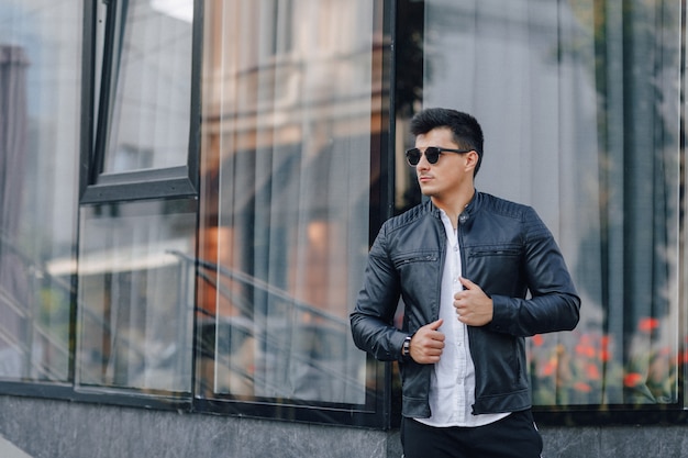 Young stylish guy in glasses in black leather jacket on glass surface