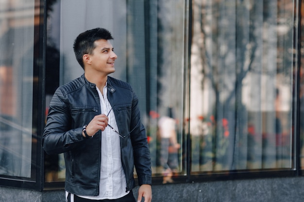 Young stylish guy in glasses in black leather jacket on glass surface