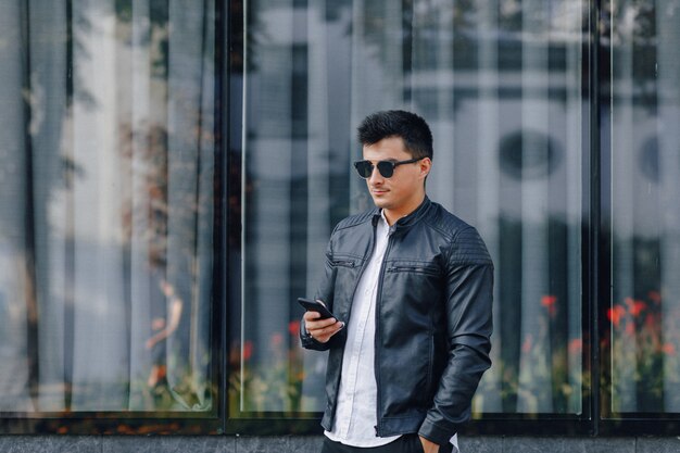 Young stylish guy in glasses in black leather jacket with phone 