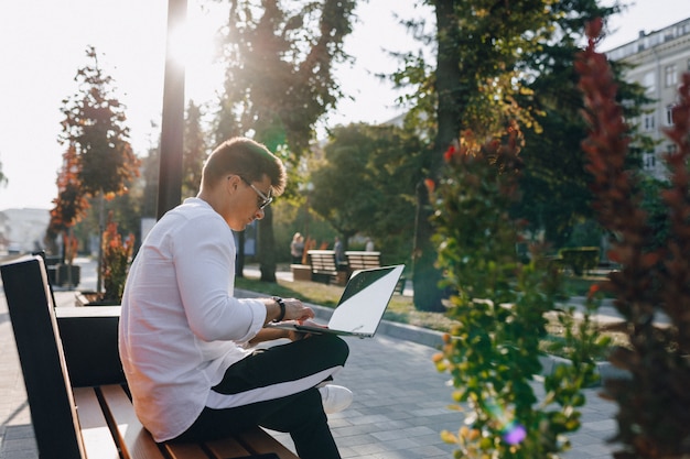 Free Photo young stylish guy in shirt with phone and notebook on bench on sunny day outdoors