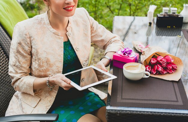 Young stylish happy woman sitting in cafe, holding tablet