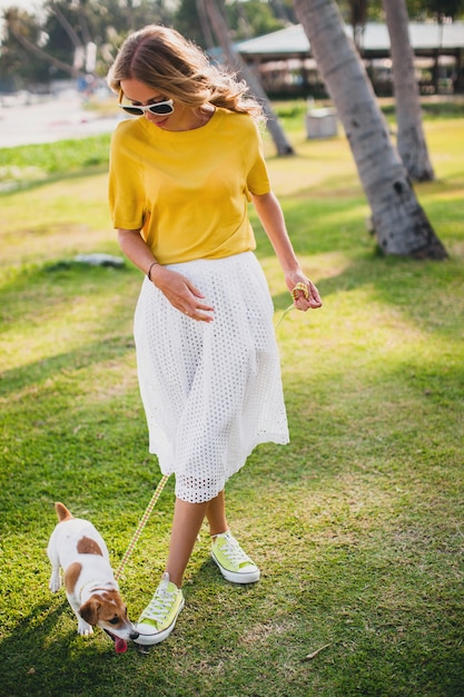 Young stylish hipster woman holding walking and playing with dog at the beach