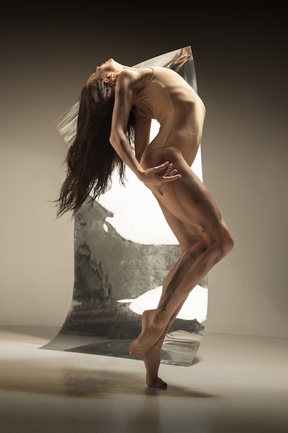 Free photo young and stylish modern ballet dancer on brown wall with the mirror and illusion reflections on surface