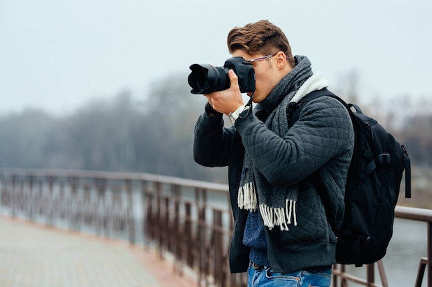 Young stylish photographer holds professional camera, taking photos.