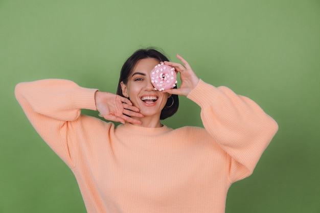 Young stylish woman in casual peach sweater  isolated on green olive wall with pink donut happy copy space