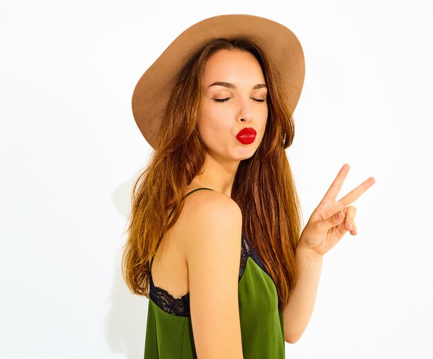 Young stylish woman model in casual summer green clothes and brown hat with red lips. Showing peace sign and giving kiss