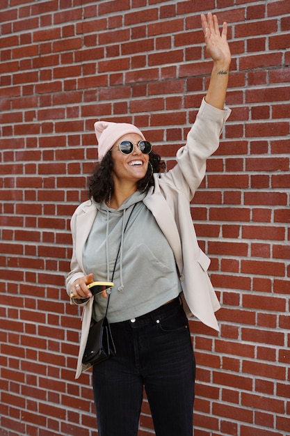 Free Photo young stylish woman using smartphone against brick wall in the city