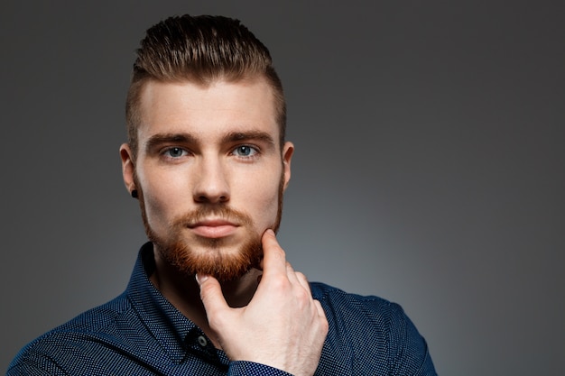 Young successful businessman posing over dark wall.