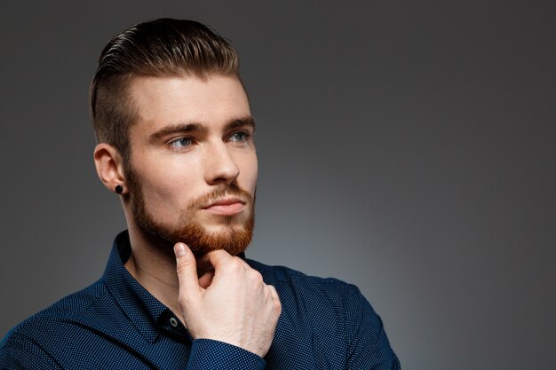 Young successful businessman posing over dark wall.