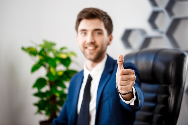 Young successful businessman showing okay at workplace.