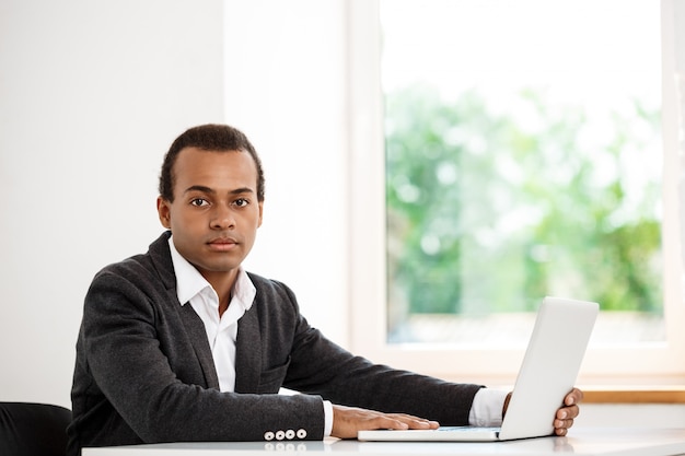 Free photo young successful businessman sitting at workplace with laptop