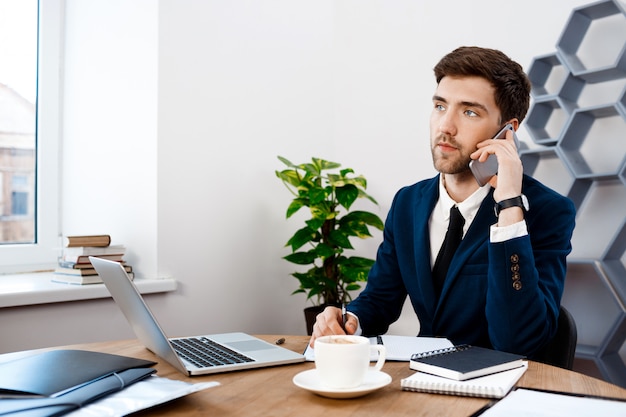 Free photo young successful businessman speaking on phone, office background.