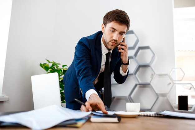 Young successful businessman speaking on phone, office background.