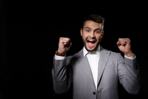 Free photo young successful businessman in suit rejoicing isolated on black