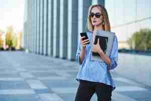 Free photo young successful businesswoman is waiting her new partner on the street with mobile phone in her hands.