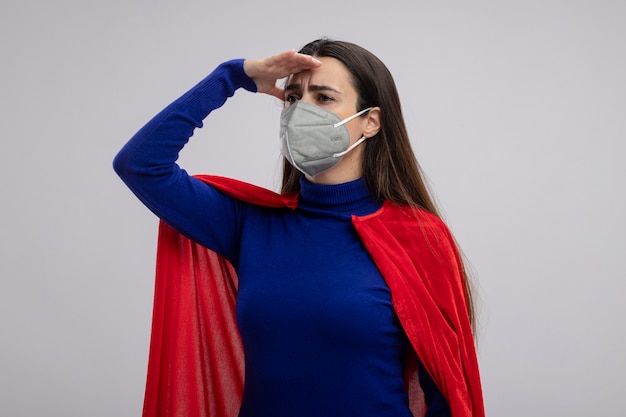 Free photo young superhero girl wearing medical mask looking at distance with hand isolated on white