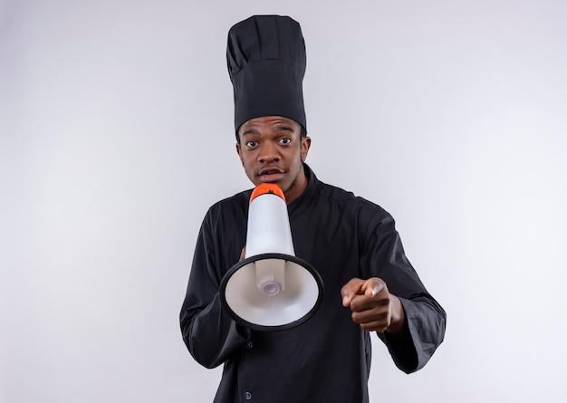 Young surprised afro-american cook in chef uniform holds loud speaker isolated on white wall