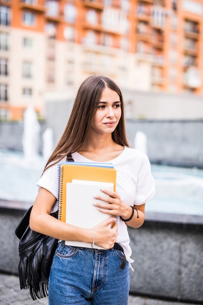 Young talented female student dressed in casual clothing walking around city. Attractive brunette woman enjoying free time outdoors