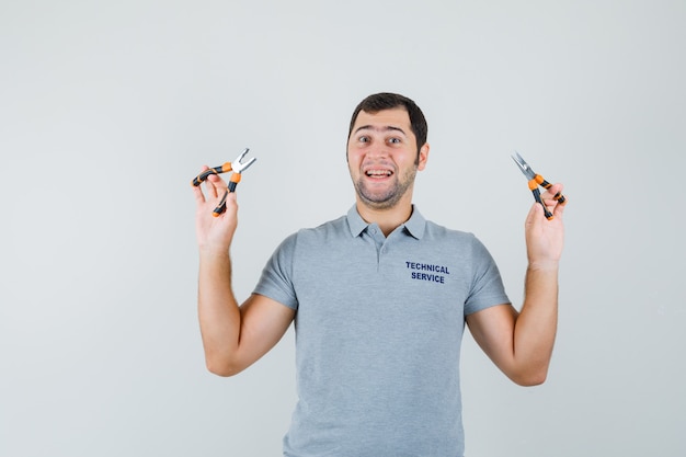 Young technician in grey uniform holding pliers in both hands and looking optimistic , front view.